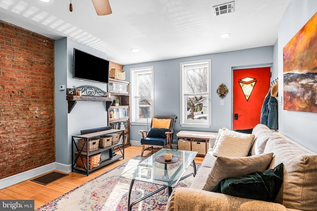 living room featuring ceiling fan, visible vents, baseboards, brick wall, and wood finished floors