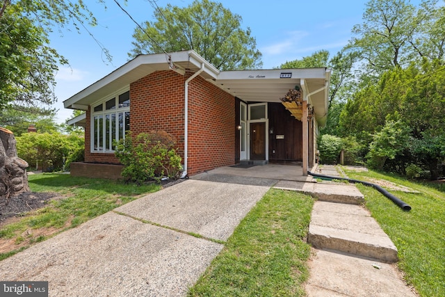 view of front of house featuring concrete driveway, brick siding, a carport, and a front yard