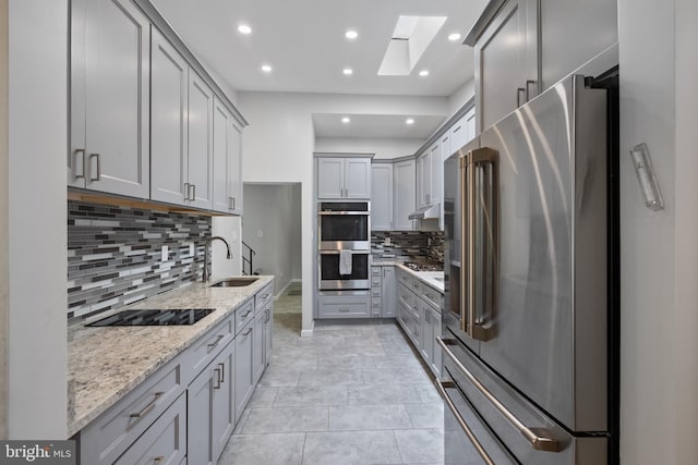 kitchen featuring appliances with stainless steel finishes, a sink, gray cabinetry, decorative backsplash, and light stone countertops