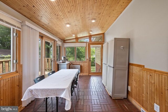 dining area featuring wainscoting, plenty of natural light, wooden walls, brick floors, and vaulted ceiling