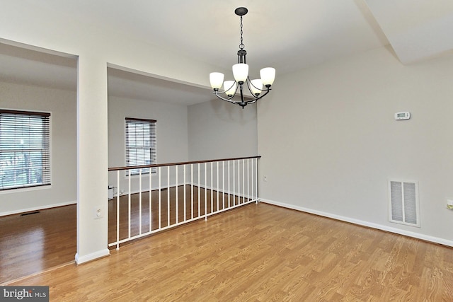 spare room featuring wood finished floors, a chandelier, and baseboards