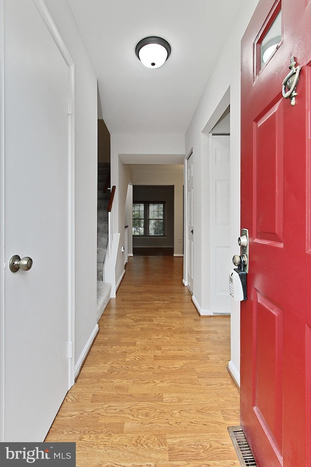 hallway featuring stairs, light wood-type flooring, and baseboards