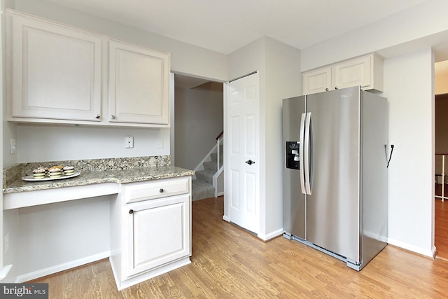 kitchen featuring stainless steel refrigerator with ice dispenser, light wood-style floors, light stone counters, and baseboards