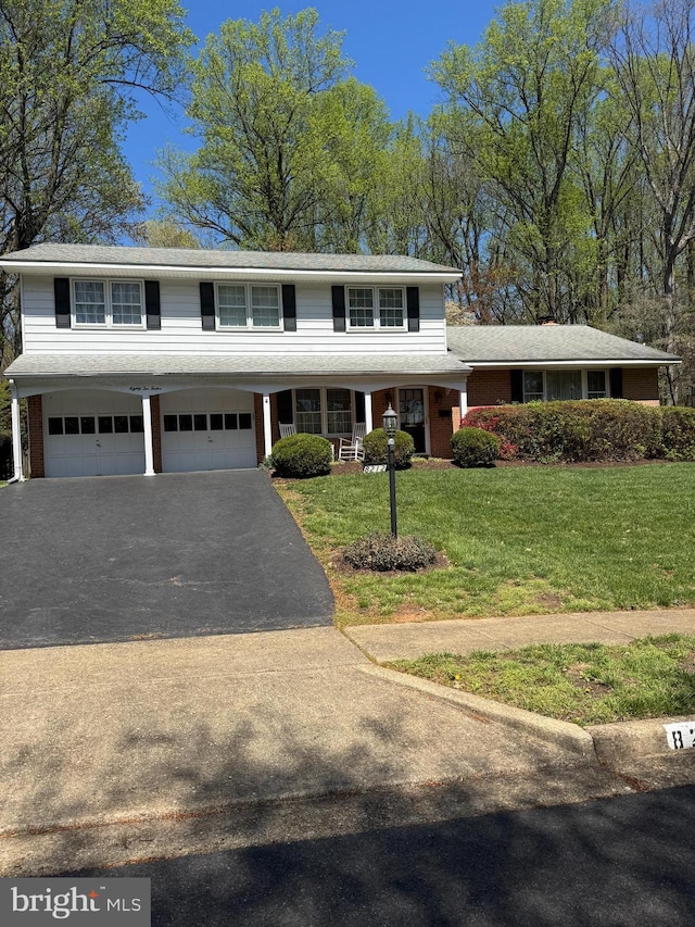 traditional home featuring a front lawn, covered porch, aphalt driveway, and an attached garage