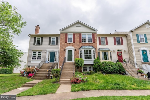 townhome / multi-family property featuring brick siding, stairs, a chimney, and a front yard