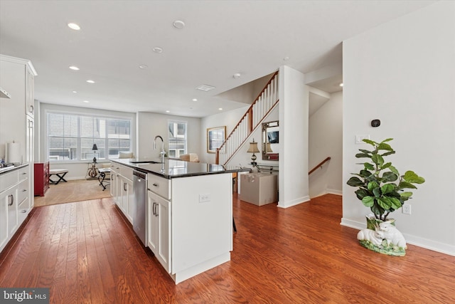 kitchen with hardwood / wood-style flooring, stainless steel dishwasher, white cabinets, a sink, and an island with sink