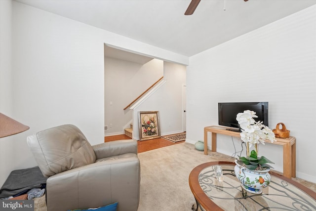 carpeted living area with ceiling fan, baseboards, and stairs