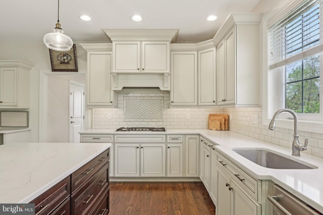 kitchen with light stone countertops, stainless steel dishwasher, decorative light fixtures, gas stovetop, and a sink