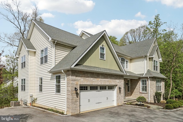 view of front facade with a shingled roof, central AC, stone siding, board and batten siding, and aphalt driveway