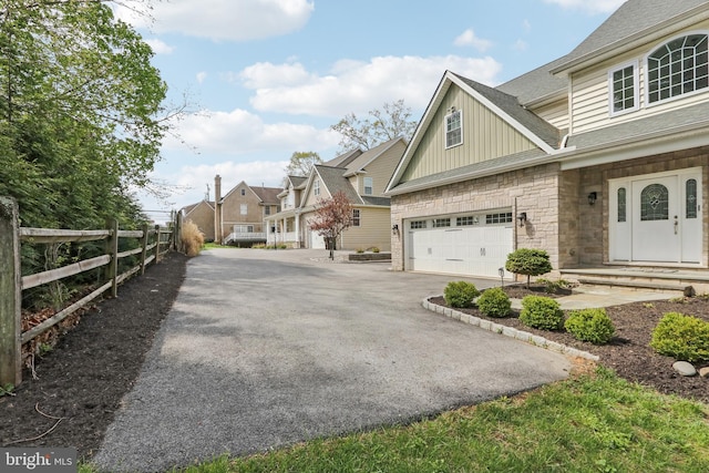 view of property exterior with driveway, stone siding, board and batten siding, roof with shingles, and fence