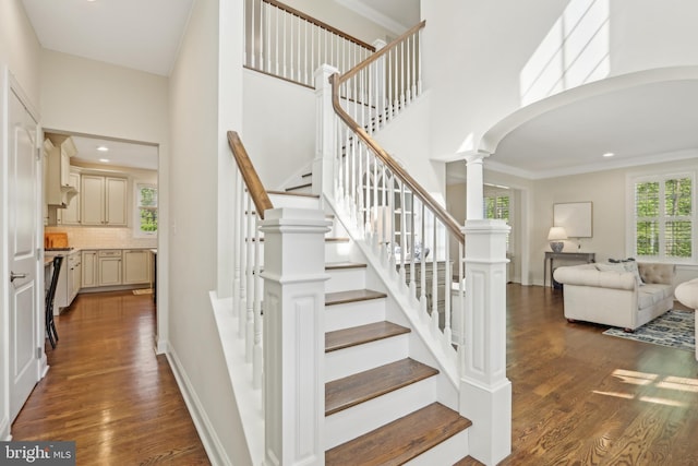 staircase with recessed lighting, a high ceiling, ornate columns, arched walkways, and wood finished floors