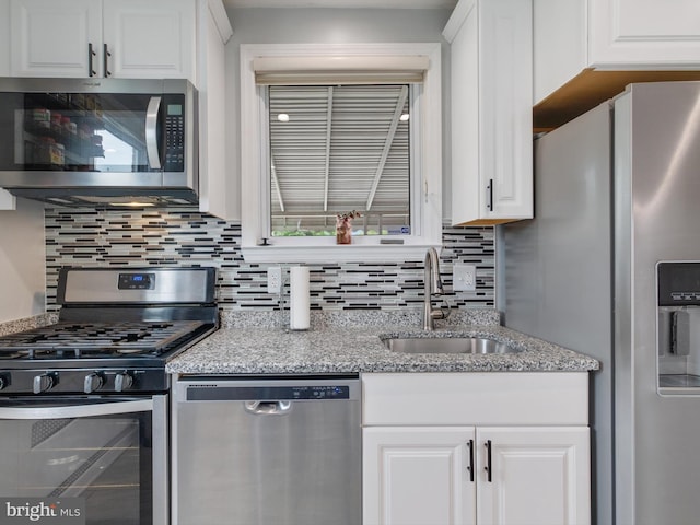 kitchen featuring light stone countertops, a sink, decorative backsplash, white cabinetry, and appliances with stainless steel finishes