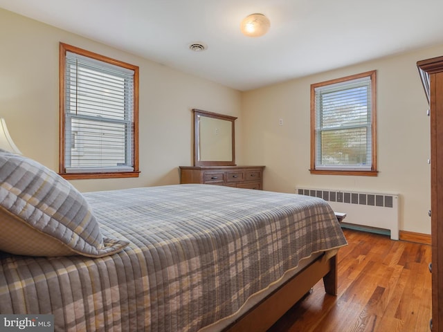 bedroom with radiator, visible vents, wood finished floors, and baseboards