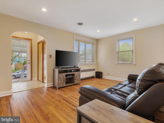 living area with radiator, arched walkways, visible vents, and a wealth of natural light