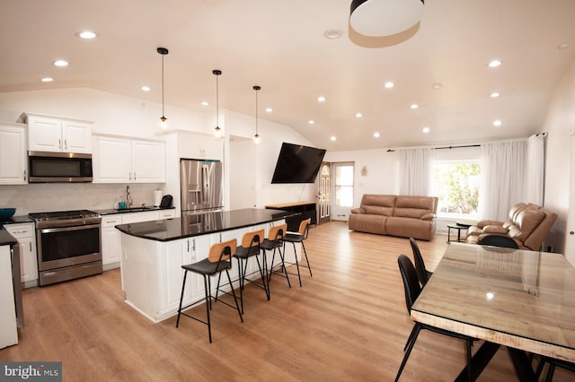 kitchen featuring a breakfast bar area, vaulted ceiling, dark countertops, and stainless steel appliances