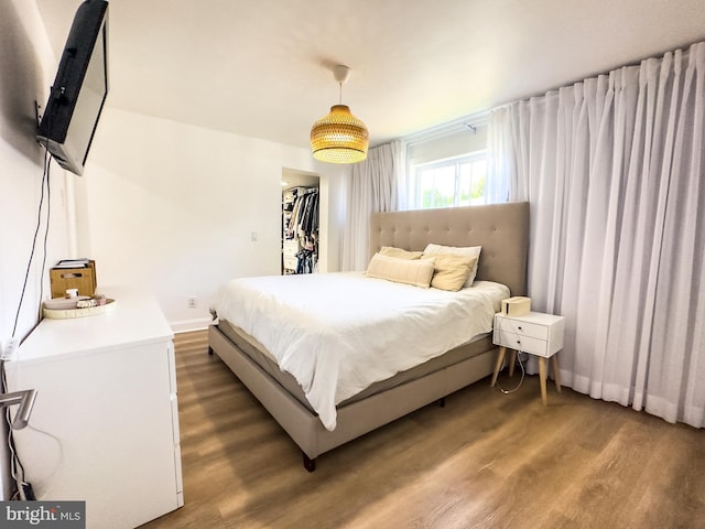 bedroom with baseboards, a walk in closet, wood finished floors, and a closet