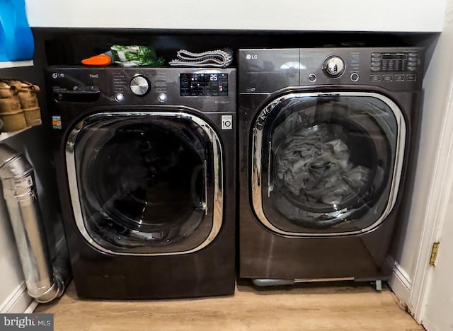 clothes washing area featuring laundry area, baseboards, wood finished floors, and washing machine and clothes dryer