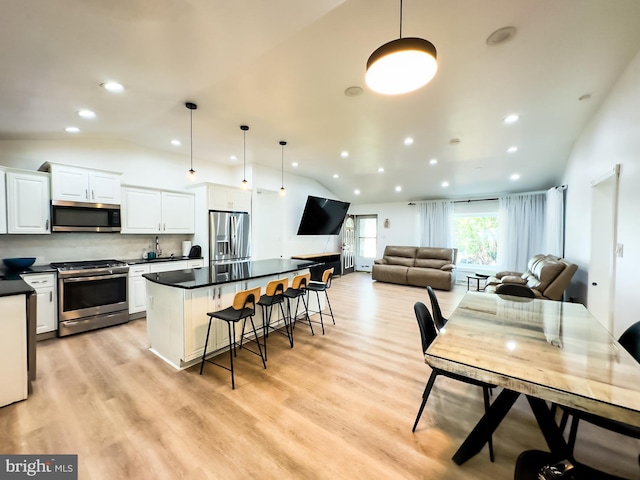 kitchen featuring dark countertops, appliances with stainless steel finishes, a breakfast bar area, and vaulted ceiling