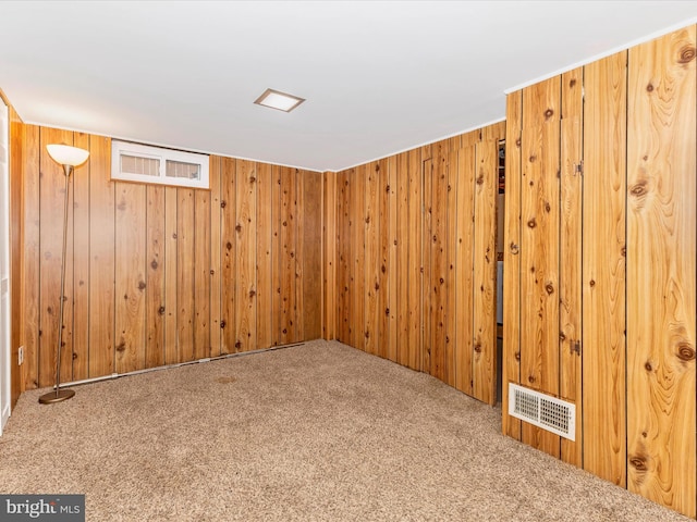carpeted empty room featuring wooden walls and visible vents