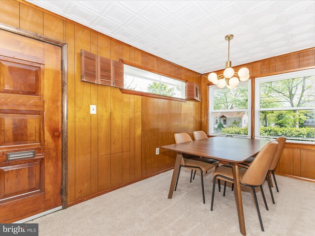 dining room with an inviting chandelier, wood walls, and light colored carpet