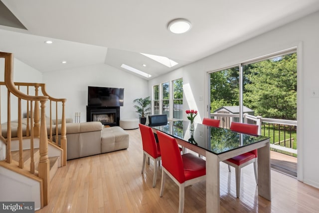 dining space featuring stairs, a glass covered fireplace, lofted ceiling with skylight, and light wood-type flooring