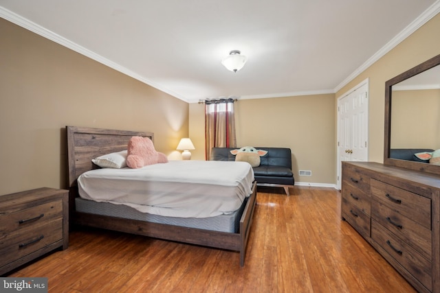bedroom with crown molding, baseboards, wood finished floors, and visible vents