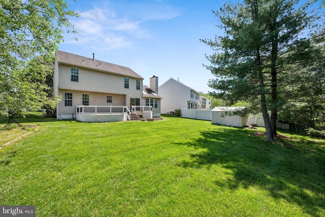 back of house featuring a lawn, a deck, an outbuilding, fence, and a storage unit