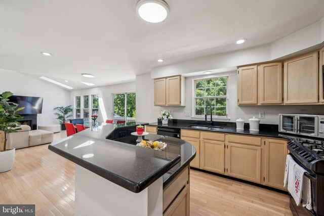 kitchen with a sink, light brown cabinets, light wood-style flooring, open floor plan, and black appliances