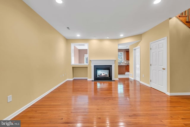 unfurnished living room with baseboards, a fireplace with flush hearth, visible vents, and light wood-style floors