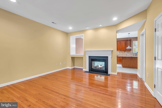 unfurnished living room with light wood-style flooring, a multi sided fireplace, recessed lighting, baseboards, and visible vents