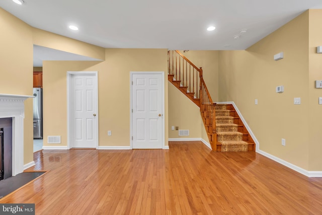 unfurnished living room with stairway, baseboards, light wood-type flooring, and visible vents