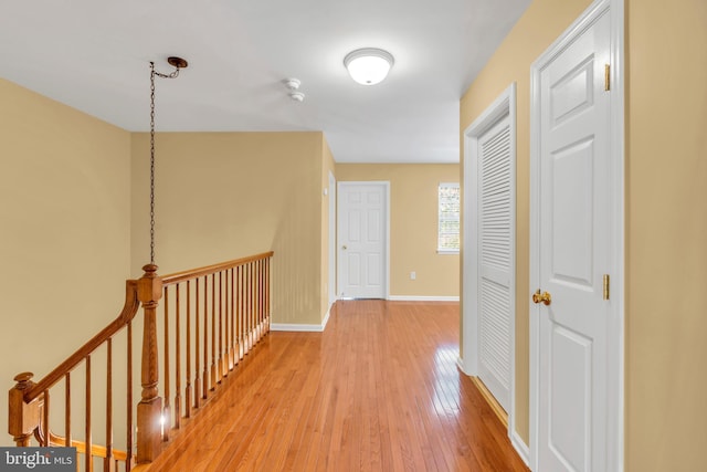 hallway featuring baseboards, light wood-style flooring, and an upstairs landing