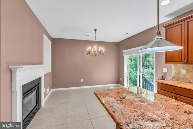 kitchen featuring brown cabinetry, pendant lighting, light stone countertops, backsplash, and a notable chandelier