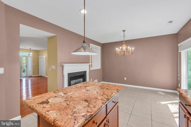 kitchen featuring light stone countertops, a notable chandelier, a glass covered fireplace, baseboards, and visible vents