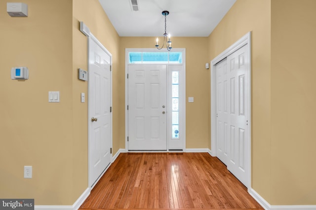 foyer with baseboards, a chandelier, light wood-style flooring, and visible vents