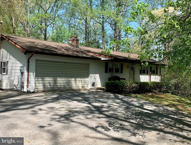 view of front of property featuring a garage, driveway, a chimney, and central AC unit