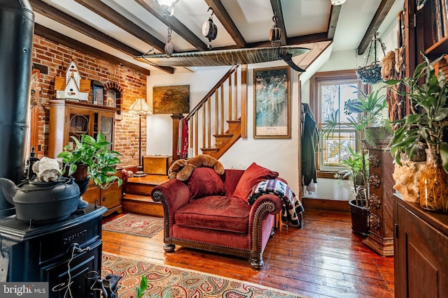 living room featuring a wood stove, stairway, beam ceiling, brick wall, and hardwood / wood-style floors
