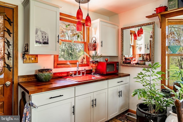 kitchen with wood counters, white cabinetry, hanging light fixtures, and a sink