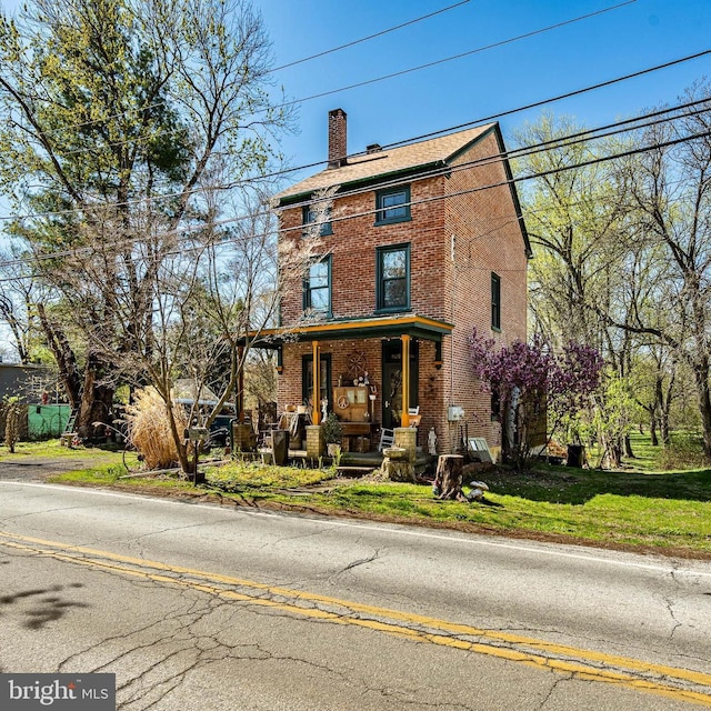 italianate-style house with a front yard, a chimney, a porch, and brick siding