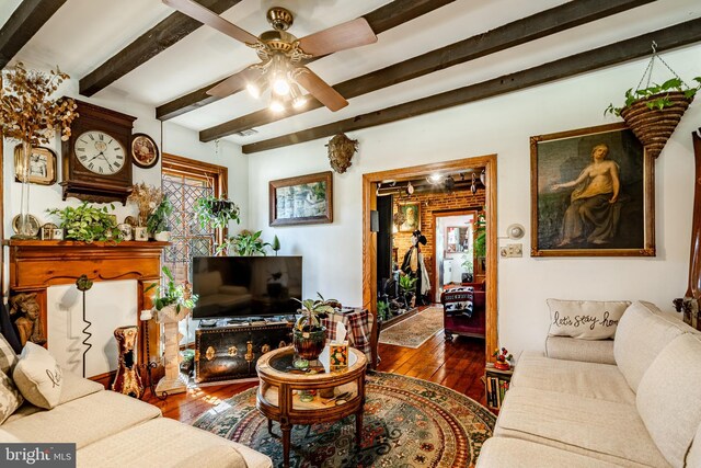 living area with beam ceiling, hardwood / wood-style floors, and a ceiling fan