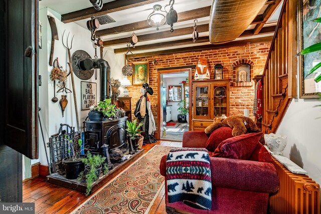 living area with a wood stove, beamed ceiling, wood-type flooring, and brick wall