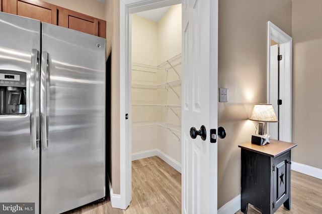 interior space with brown cabinets, light wood-type flooring, stainless steel fridge, and baseboards
