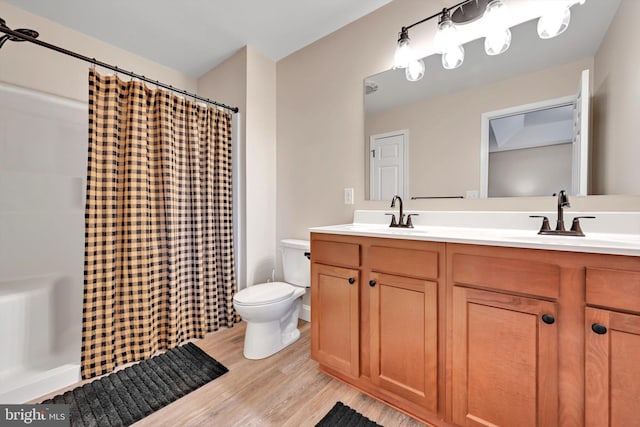 bathroom featuring wood finished floors, toilet, double vanity, and a sink