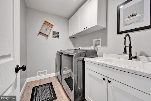 clothes washing area with independent washer and dryer, cabinet space, light wood finished floors, a sink, and visible vents