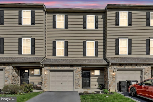 townhome / multi-family property with stone siding, driveway, and a garage