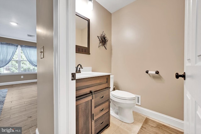 bathroom featuring visible vents, baseboards, toilet, wood finished floors, and vanity
