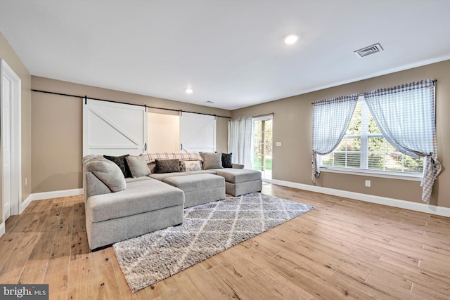 living room featuring recessed lighting, light wood-style flooring, a barn door, baseboards, and visible vents
