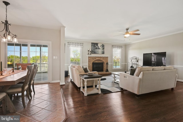 living area featuring a ceiling fan, crown molding, a brick fireplace, dark wood finished floors, and baseboards