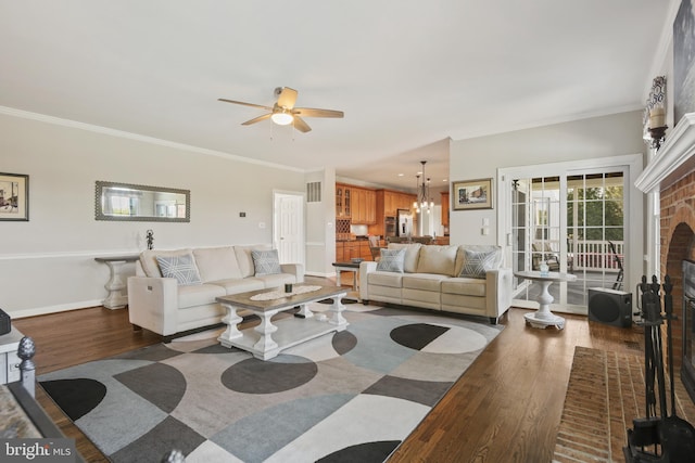 living room with visible vents, ornamental molding, a brick fireplace, wood finished floors, and ceiling fan with notable chandelier