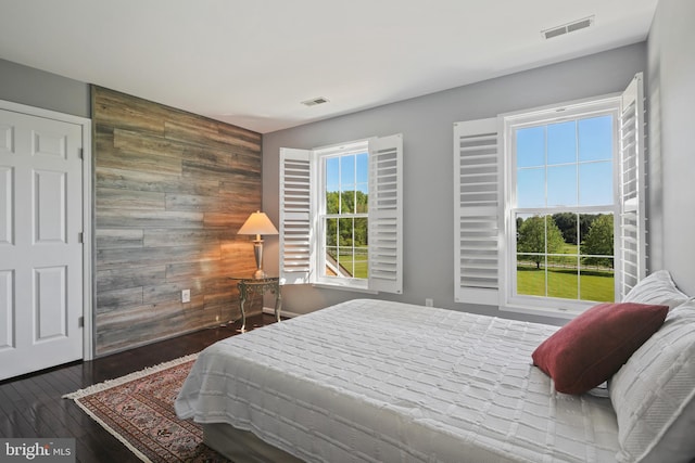 bedroom with visible vents, an accent wall, wooden walls, and wood finished floors